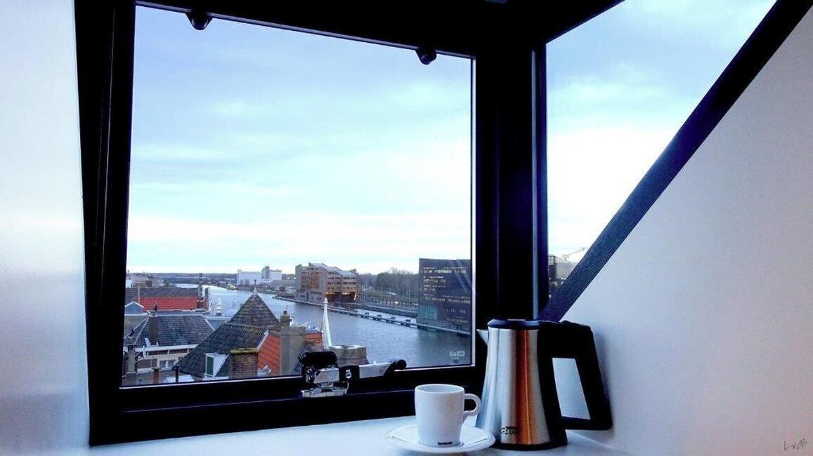 A window with a view of a cityscape, a white cup, and a silver object on the windowsill.