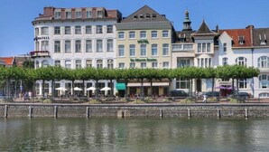 A waterfront hotel with a row of trees, a stone wall, and a clear view of the water.