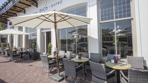 An outdoor seating area with wicker chairs and tables, umbrellas, and potted plants.