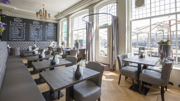 A restaurant with a menu board, cushioned seating, and large windows.