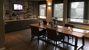 A modern dining area with a long table, chairs, a television, and shelves with various items. - Fletcher Hotel Valkenburg (Valkenburg aan de Geul)