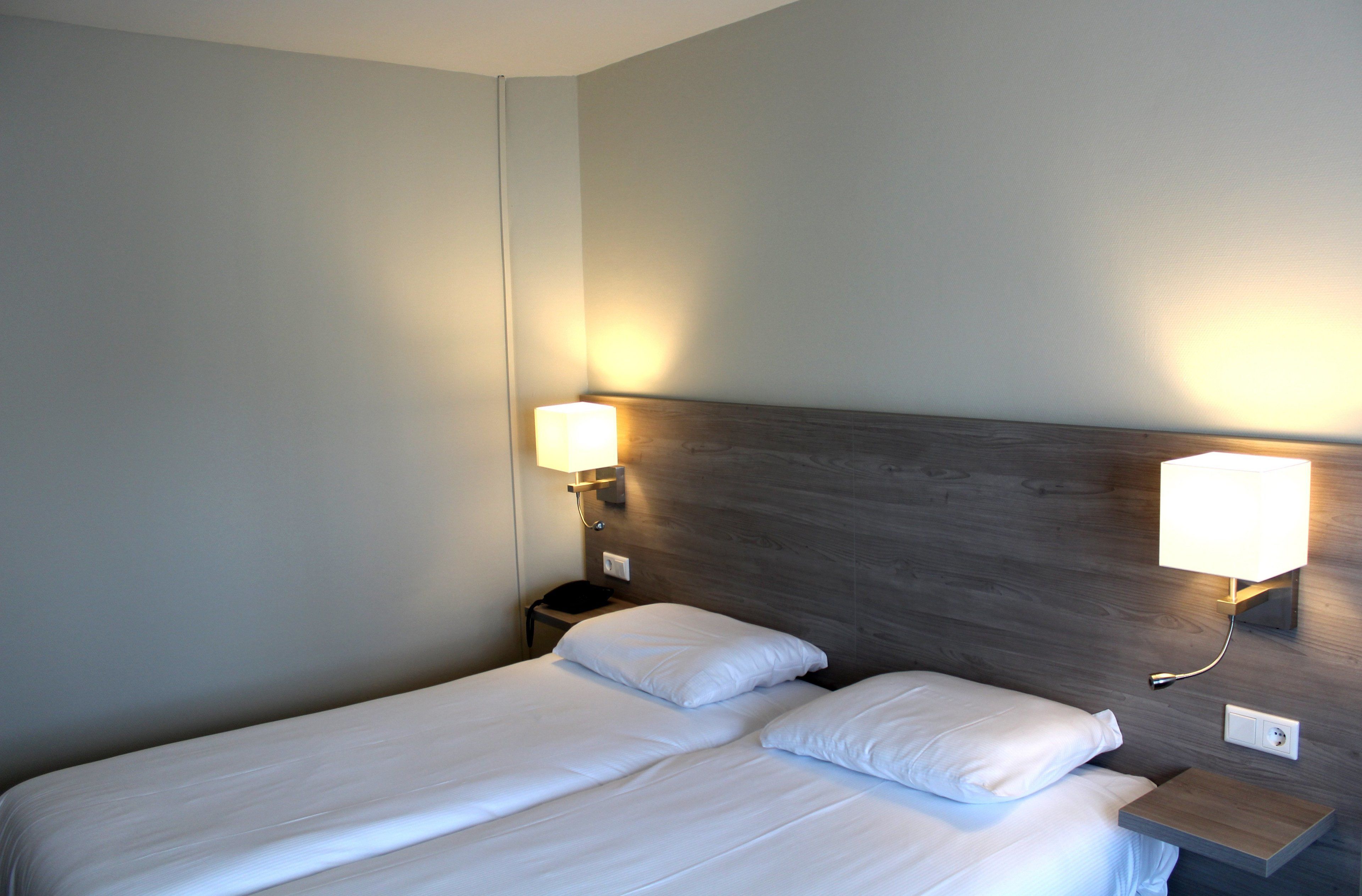 Una habitación de hotel con una cama bien hecha, dos lámparas de noche y un cabecero de madera.