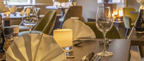 A dining table set with a candle, a glass, and cutlery.