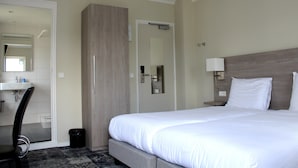 A hotel room with a bed, a bedside table with a lamp, a mirror, a wardrobe, and a bathroom with a sink and mirror. - Fletcher Hotel Valkenburg (Valkenburg aan de Geul)