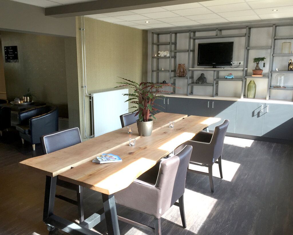 A modern dining area with a wooden table and chairs, a potted plant, and a kitchen area with a TV and shelving.