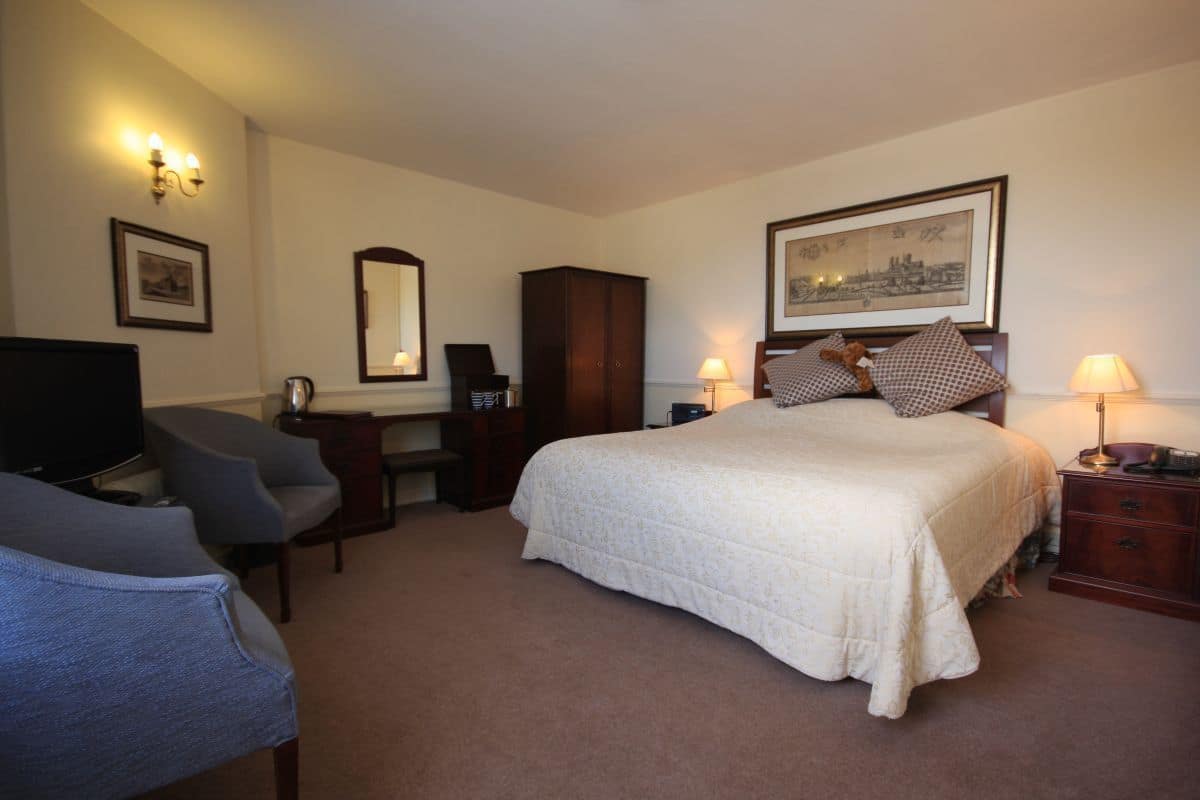 A hotel room with a bed, desk, chair, television, wardrobe, and a framed picture on the wall.