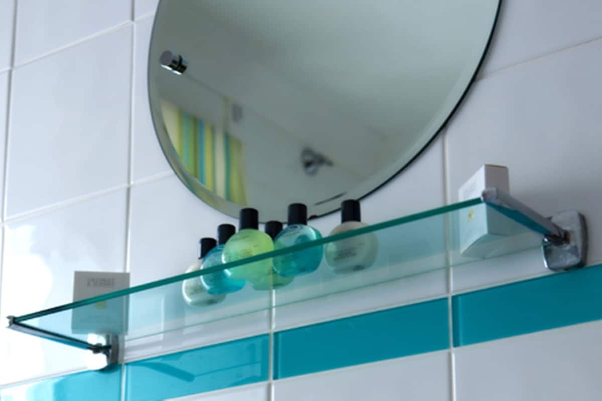 A bathroom with a glass shelf holding toiletries and a mirror on the wall.
