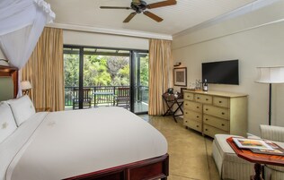 Un dormitorio amplio con una cama grande, un escritorio, una televisión y un balcón con vistas a zonas verdes.