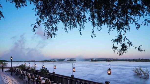 A deck with chairs and tables overlooking a body of water, with hanging lanterns providing light. - Royal Livingstone Victoria Falls Zambia Hotel by Anantara (Livingstone)