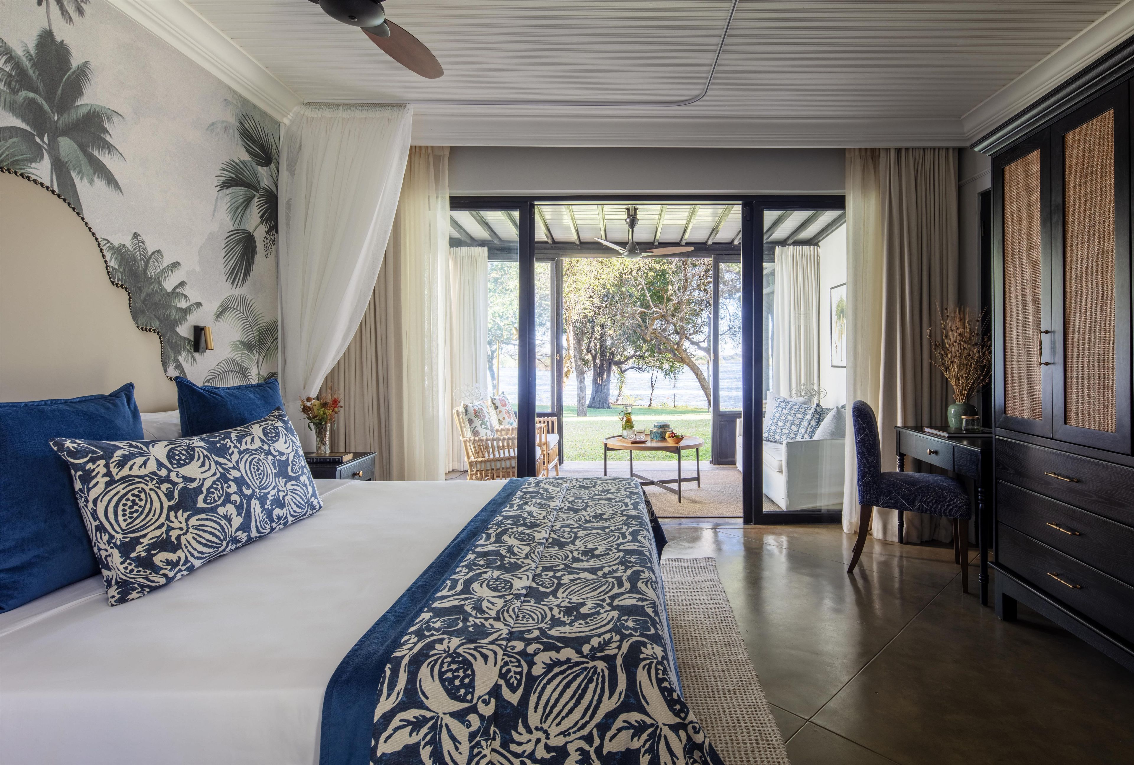 Habitación de hotel con una cama grande, zona de comedor con mesa y sillas, y vistas al exterior.