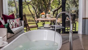 A spa area with a bathtub, a table with a bottle of champagne, and a view of trees. - Royal Livingstone Victoria Falls Zambia Hotel by Anantara (Livingstone)