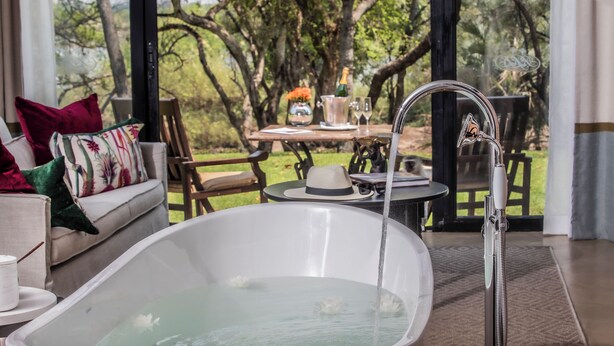 Un área de spa con una bañera, una mesa con una botella de champán y vistas a árboles.