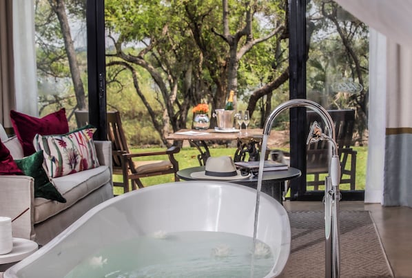 Un área de spa con una bañera, una mesa con una botella de champán y vistas a árboles.