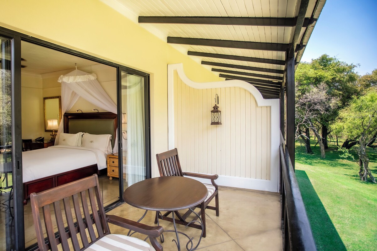Un balcone con un letto, un tavolo e sedie, affacciato su un giardino curato.