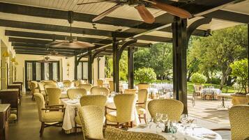 Un restaurante con mesas al aire libre, cubierto por un techo y rodeado de vegetación.