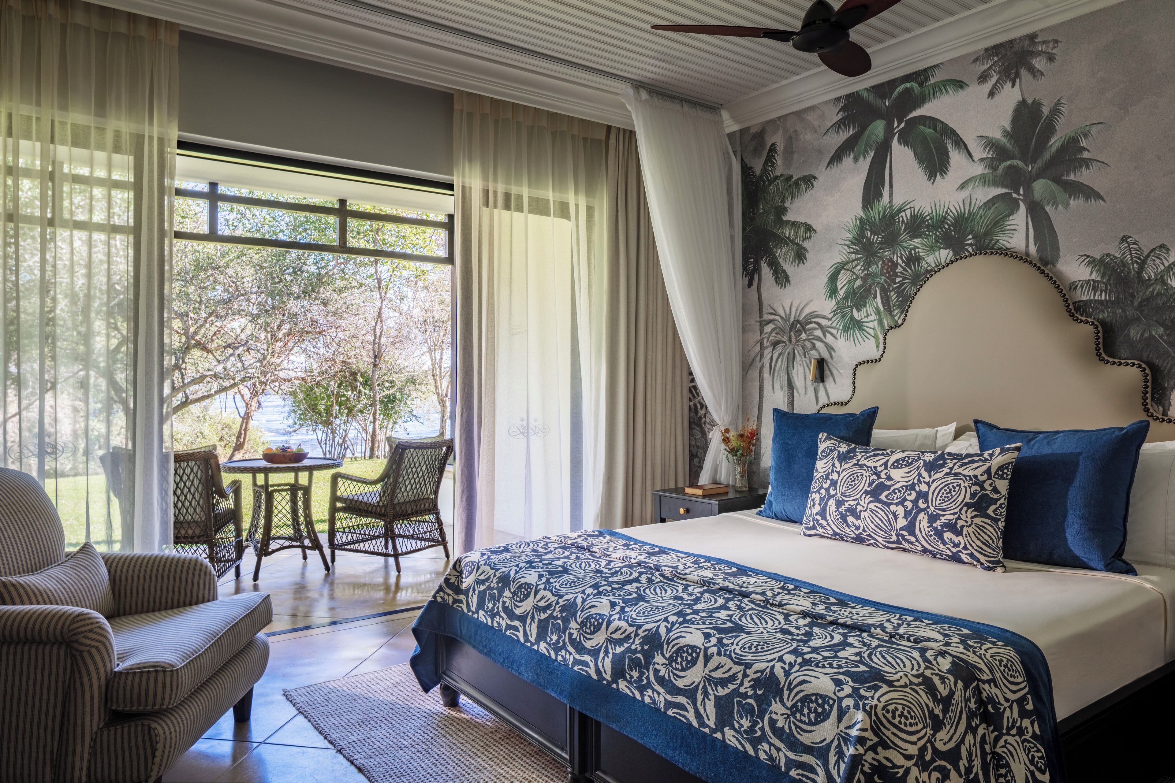 A hotel room with a bed, a dining area with a table and chairs, and a view of the outdoors.