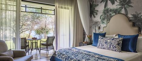 A hotel room with a bed, a dining area with a table and chairs, and a view of the outdoors.