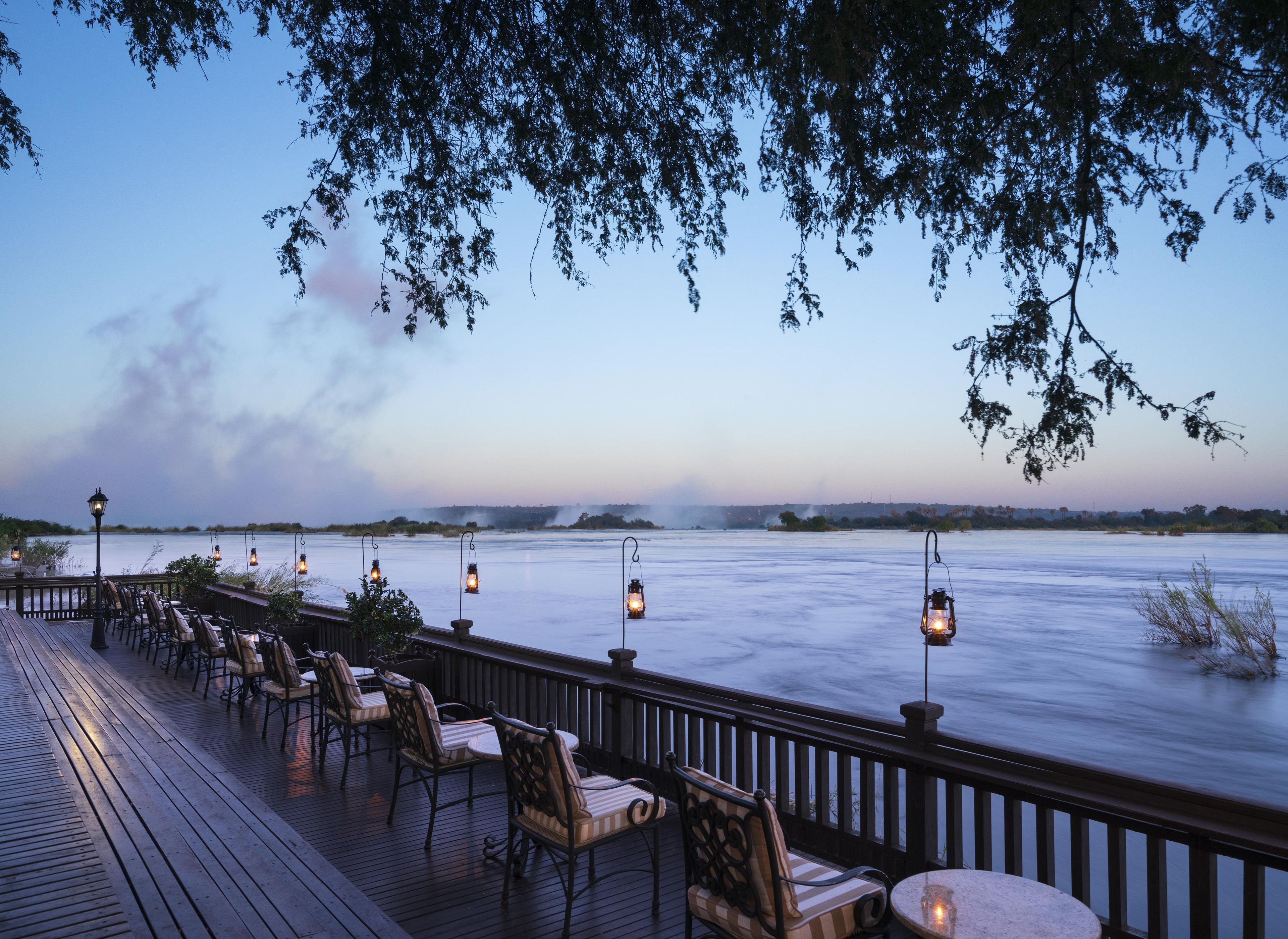 A deck with chairs and tables overlooking a body of water, with lanterns providing light.