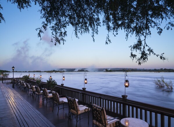 A deck with chairs and tables overlooking a body of water, with lanterns providing light.