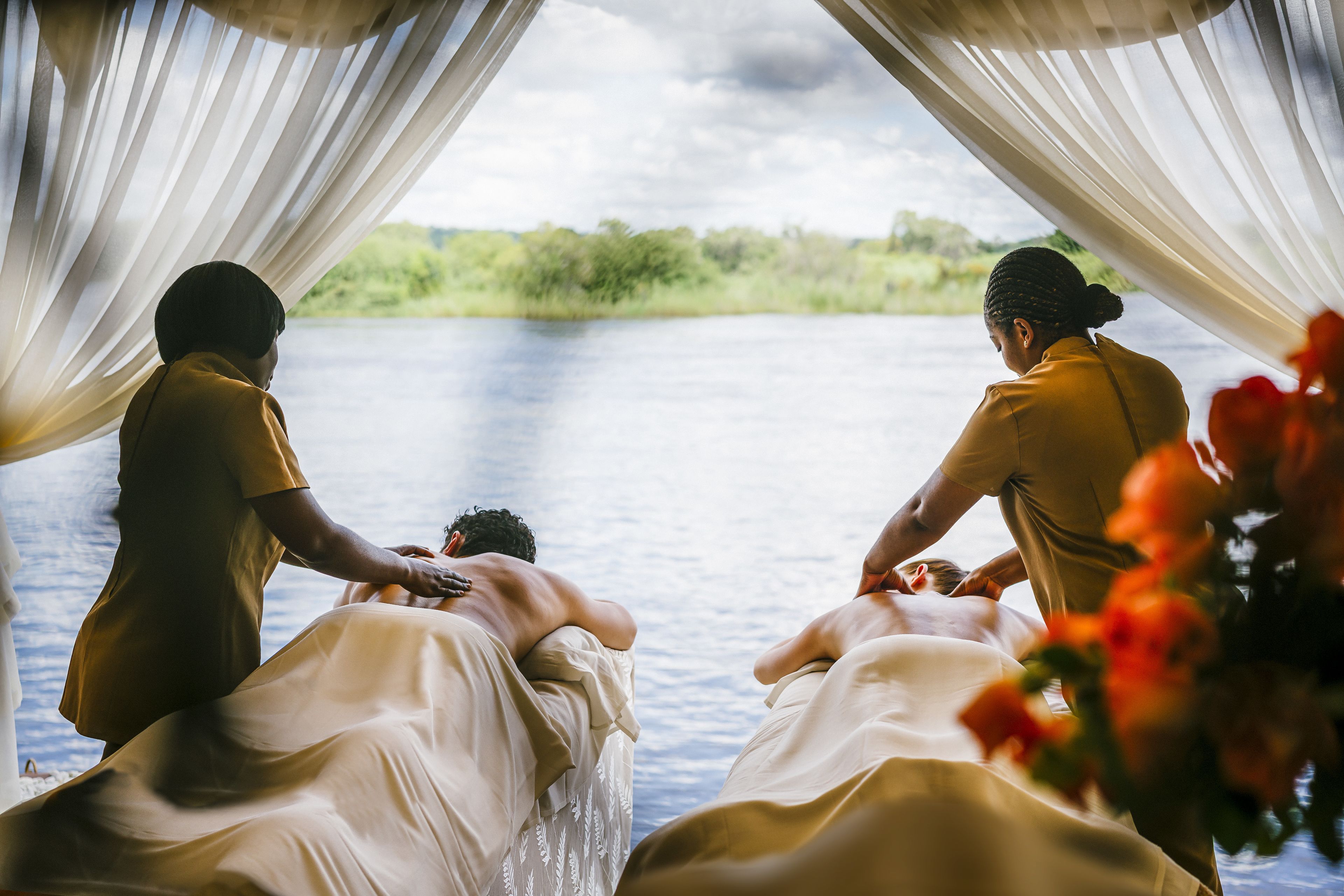 Una pareja recibiendo un masaje junto a un lago, con vistas a la vegetación y al agua.
