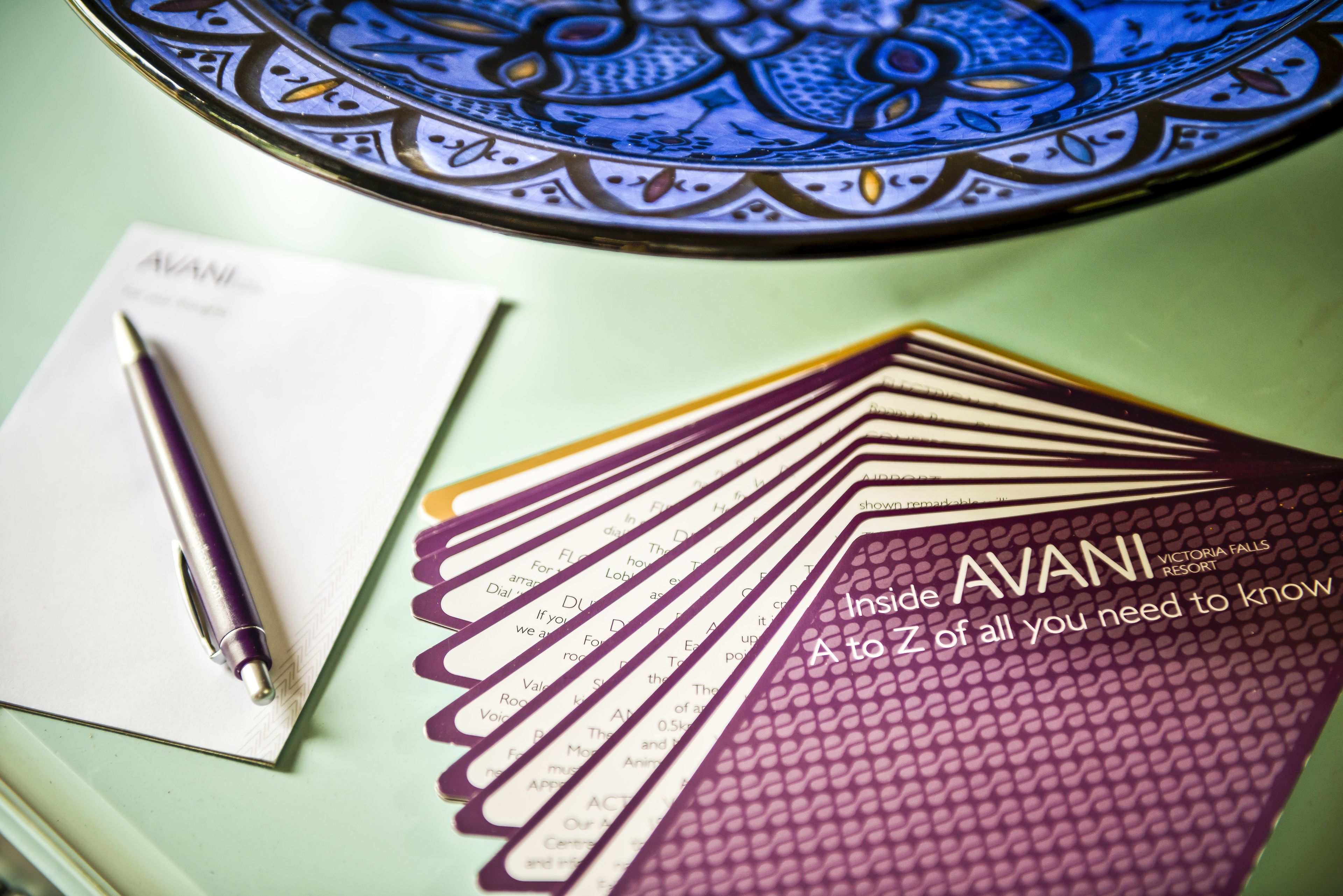 A stack of AVANI cards and a pen on a table with a decorative plate.