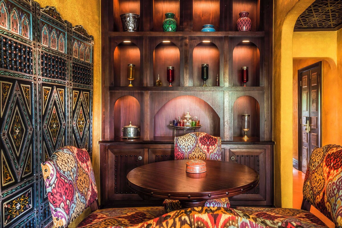 A traditional Moroccan interior with ornate wood paneling, a central round table, and patterned cushions.