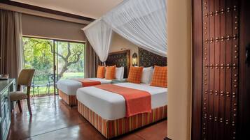 Une chambre d’hôtel avec deux lits, un bureau et une grande fenêtre donnant sur des arbres.