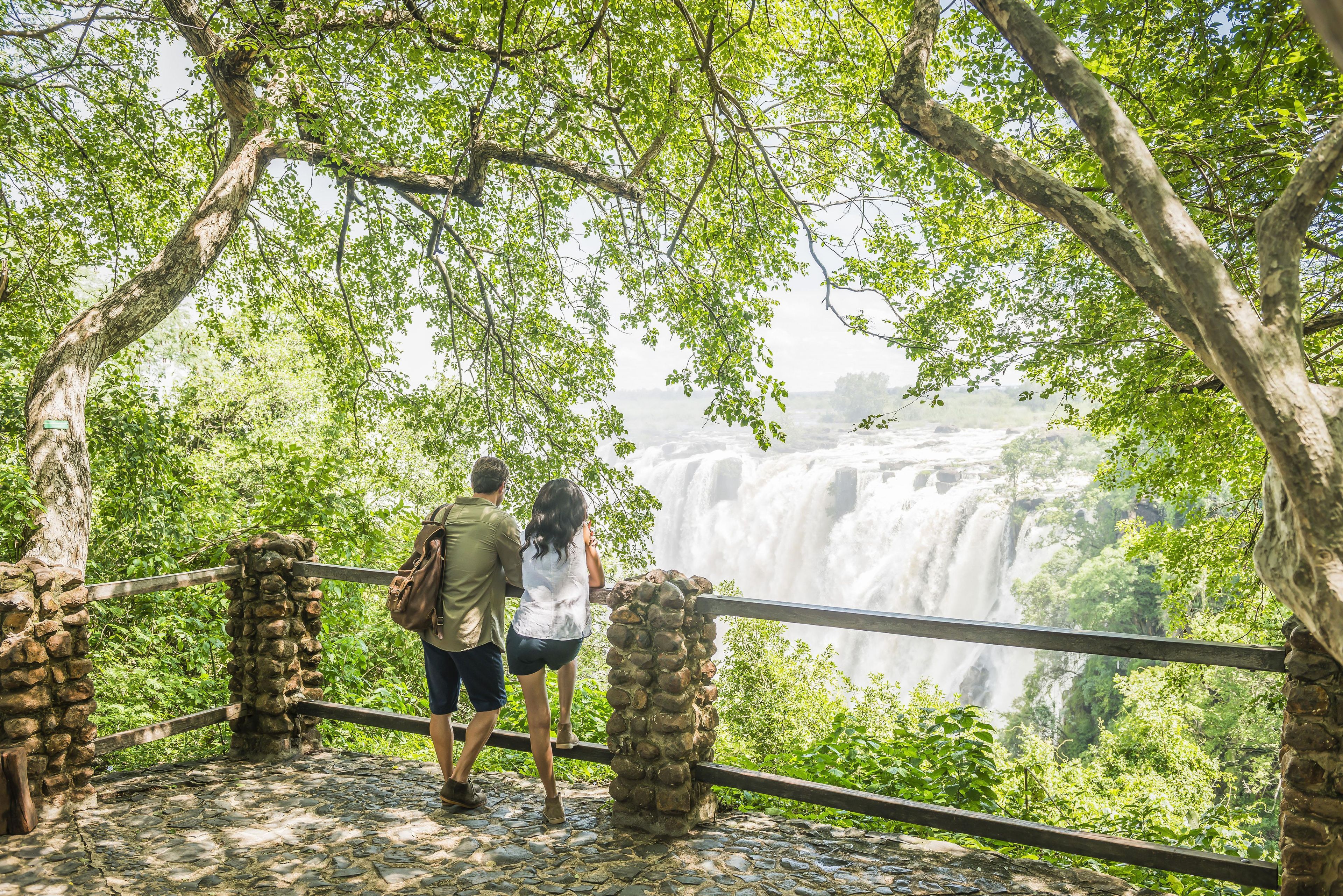A stone pathway leading to a viewing platform with a railing, overlooking a waterfall.