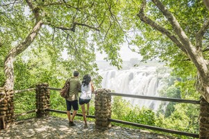 Een pad van stenen dat leidt naar een uitkijkpunt met een hek, met uitzicht op een waterval.