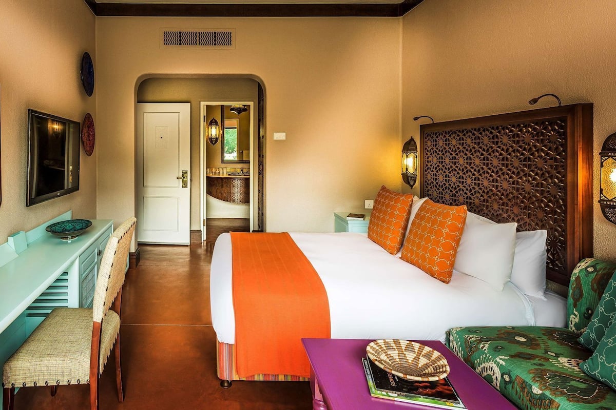 A hotel room with a bed, a desk, a chair, a small table, and a decorative wall panel.