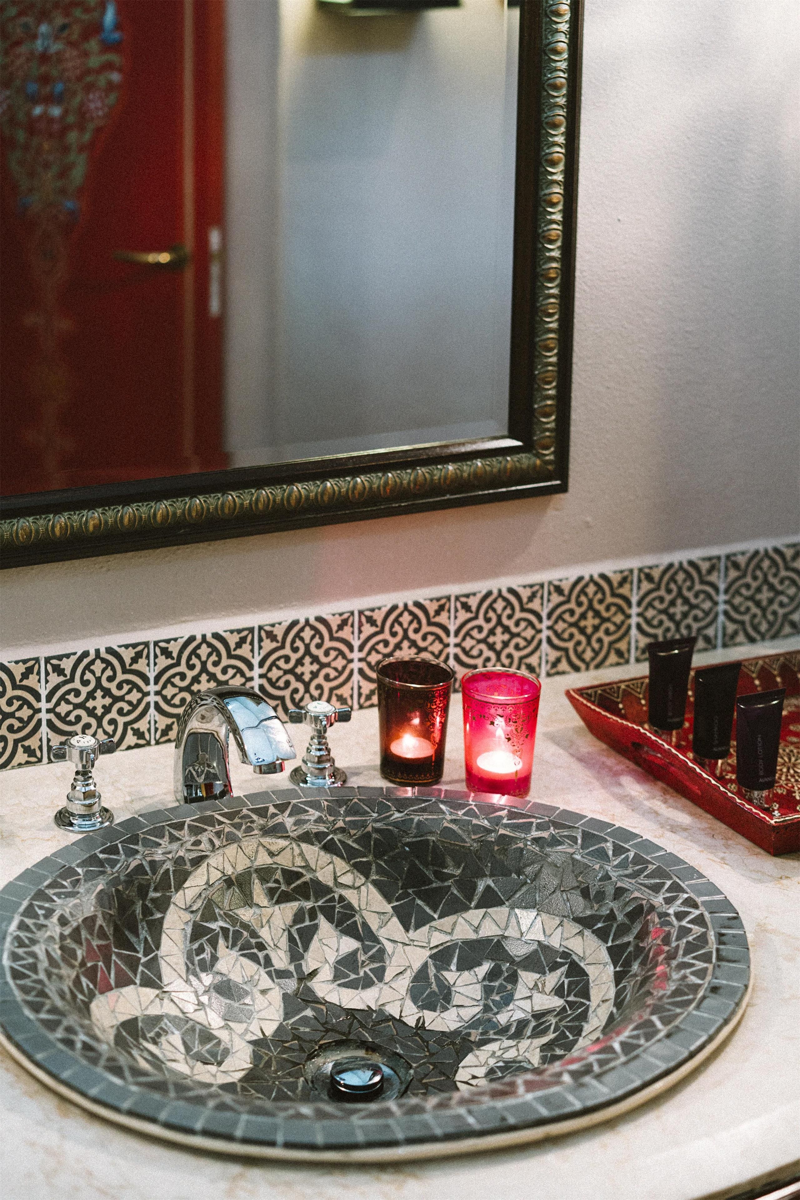 Un baño con un lavamanos de mosaico redondo, un espejo con marco decorativo y un salpicadero de azulejos.