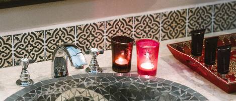 A bathroom with a round mosaic sink, a mirror with a decorative frame, and a tiled backsplash.