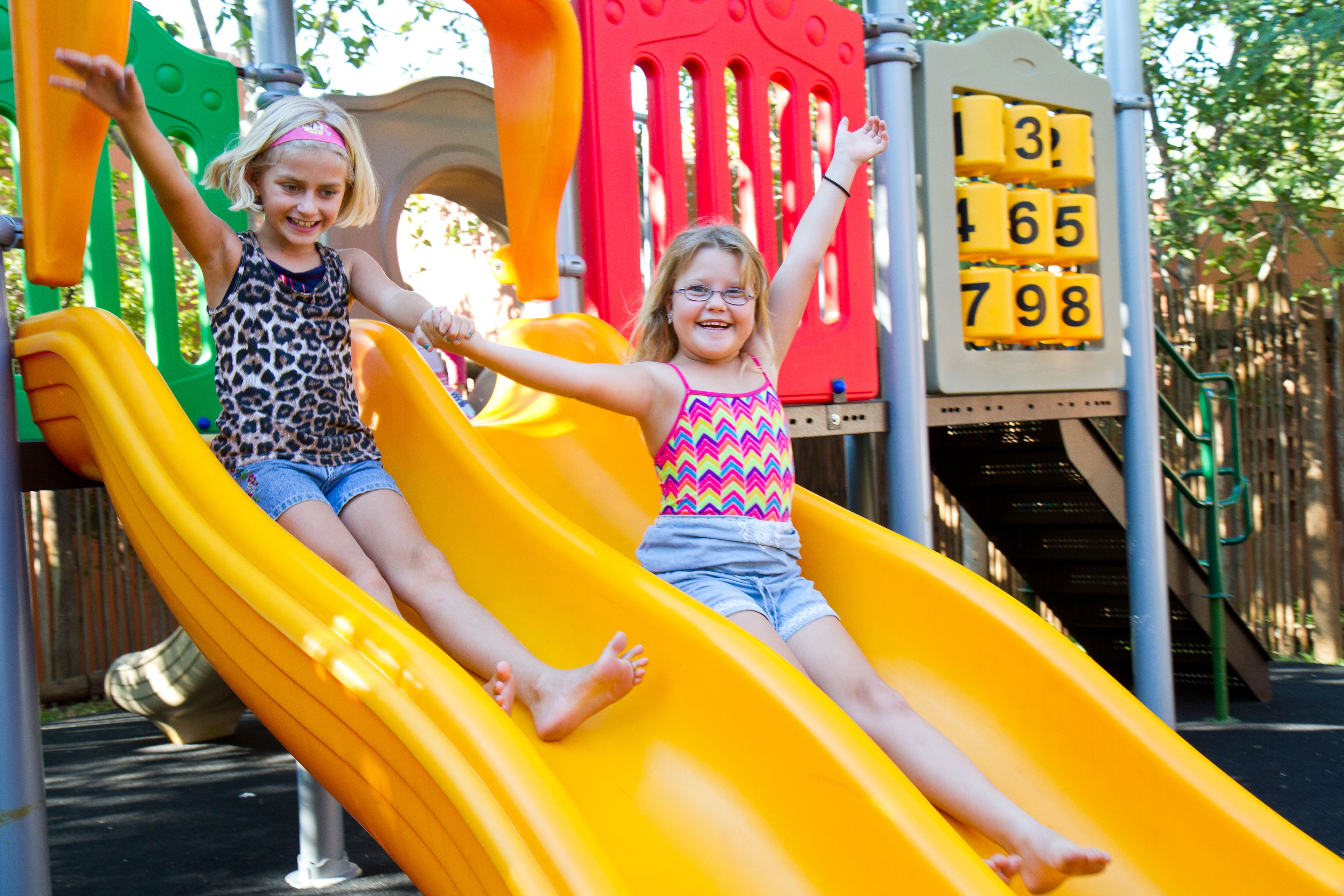Two children sliding down a yellow slide at a playground.