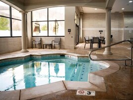 Una piscina interior con límite de profundidad de 90 centímetros, rodeada de suelo de baldosas, con zona de estar y ventanas amplias.