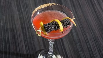 A cocktail in a stemmed glass with a sugar rim, garnished with blackberries and a lemon slice.
