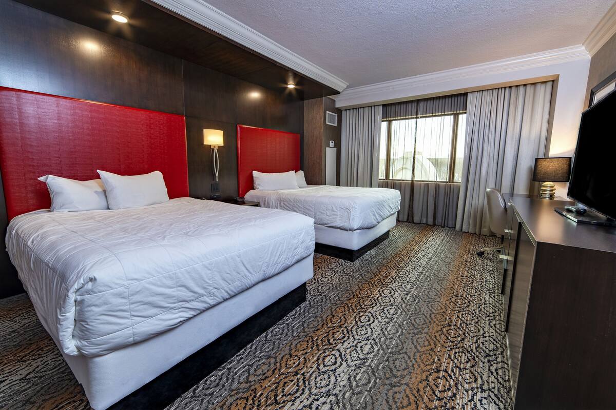 A hotel room with two beds, a desk, a TV, and a large window with curtains.