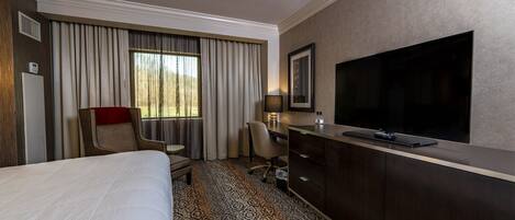 A hotel room with a bed, a desk with a chair, a television, and a window with curtains.