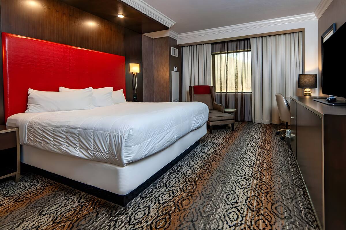 A hotel room with a large bed, a desk with a computer, a chair, and a window with curtains.