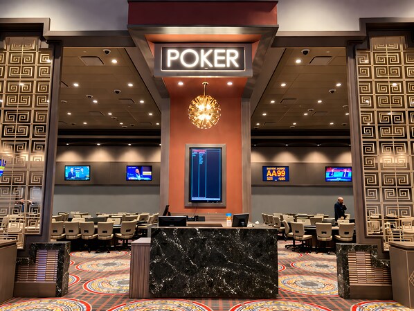 A poker room with a marble reception desk, multiple gaming tables, and overhead monitors displaying game information.