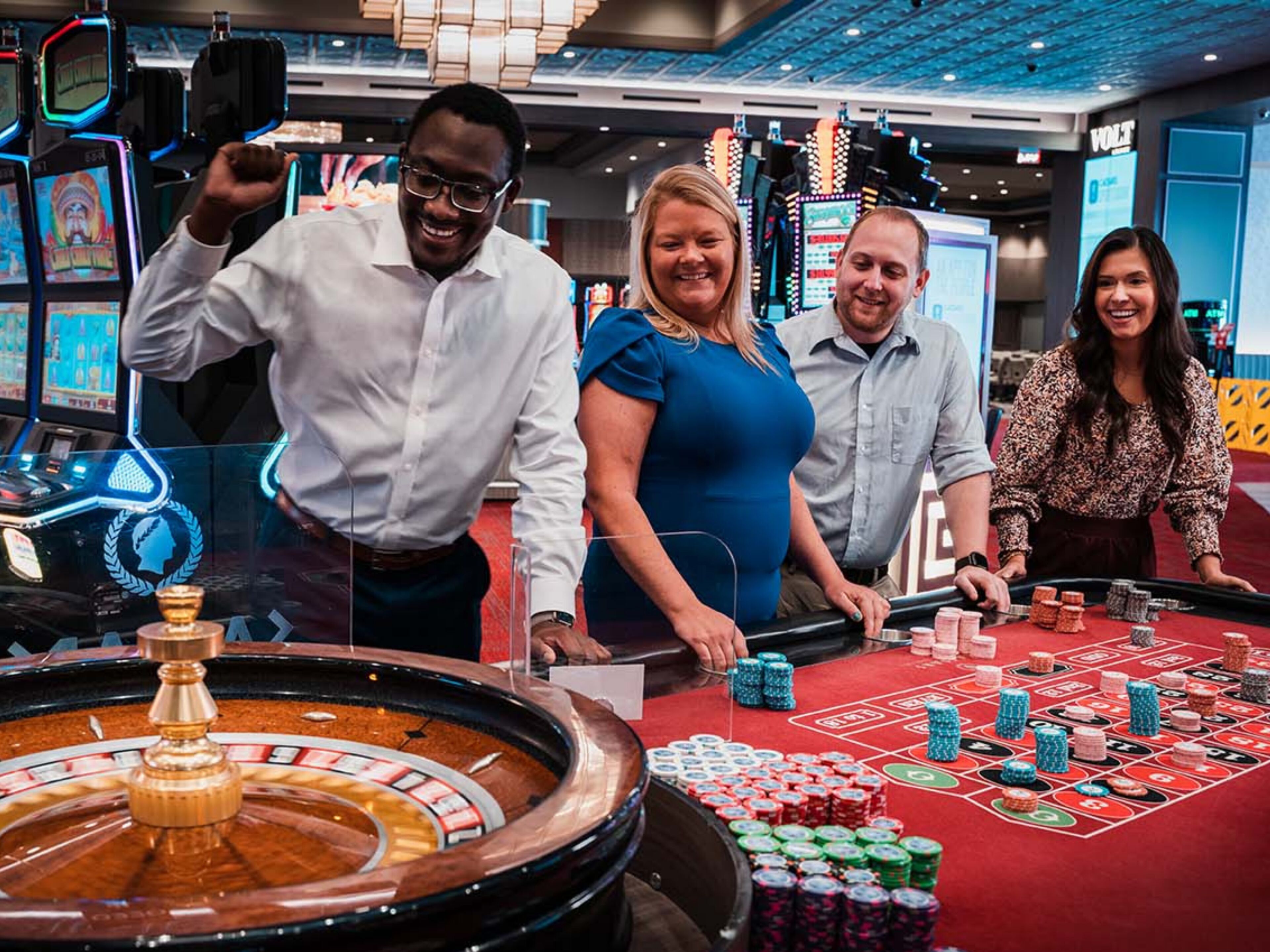 A casino floor with a roulette table, poker tables, and slot machines.