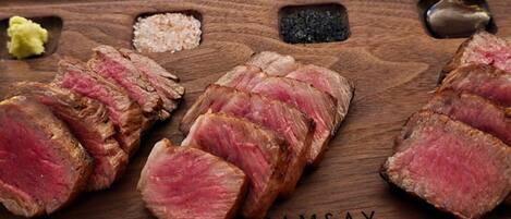 Una tabla de madera con carne de res en rodajas, sal y pimienta.
