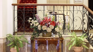 A lobby with a marble floor, a wooden console table with a vase of flowers, and a staircase with a metal railing. - Hotel Torino (Rome)