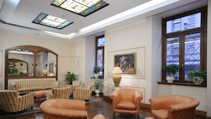 A spacious living room with striped sofas, a coffee table, and a fireplace. There are two large windows with views of the outside. - Hotel Torino (Rome)