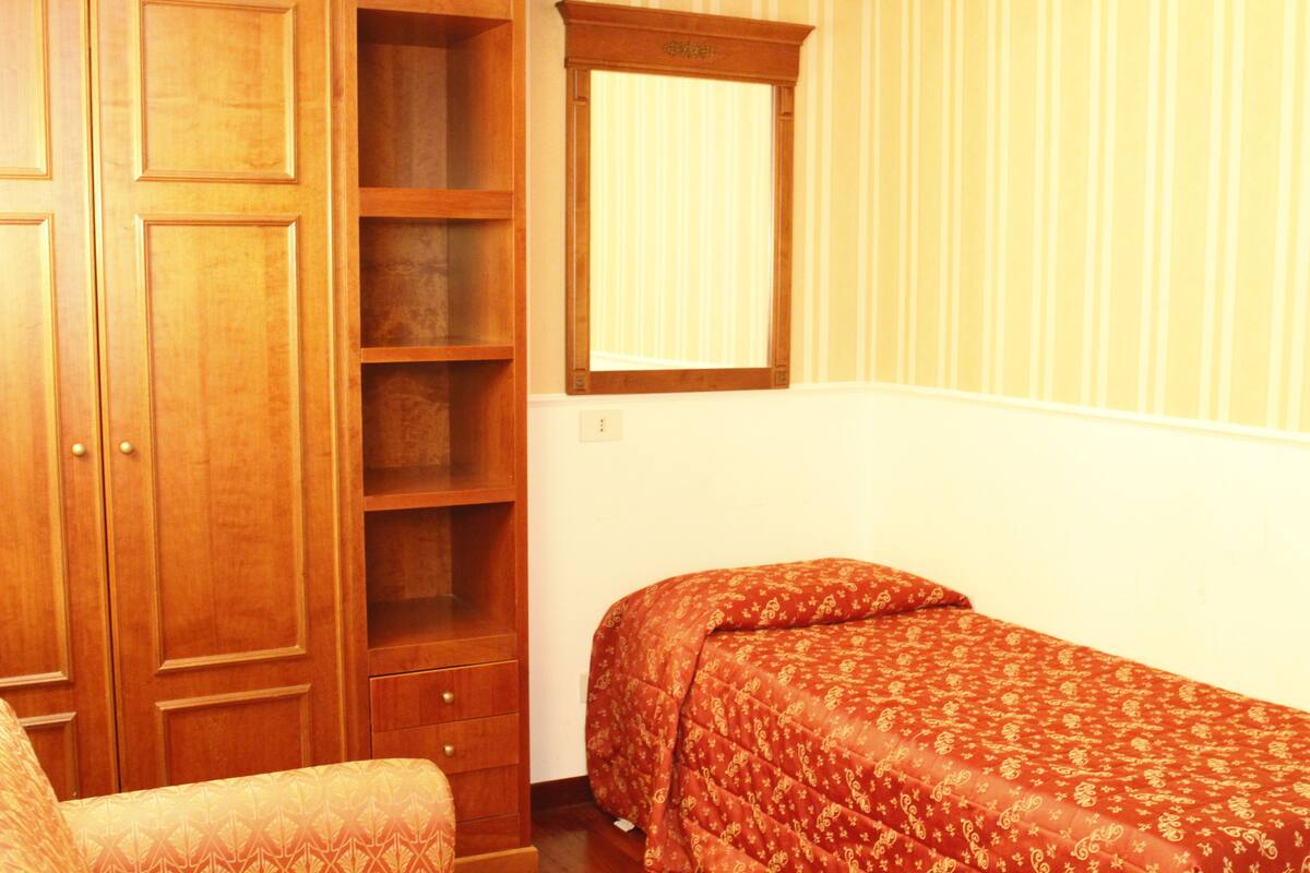 A bedroom with a wooden wardrobe, a mirror, and a bed with a patterned bedspread.