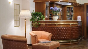 A lobby with a curved reception desk, a plush armchair, a floor lamp, and a potted plant. - Hotel Torino (Rome)