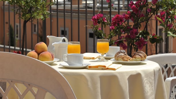 A table set with breakfast items, including fruits, croissants, and orange juice, overlooking a cityscape with historical buildings. - Hotel Torino (Rome)