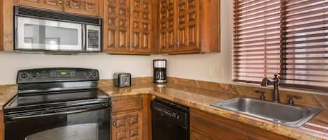 A kitchen with wooden cabinets, a microwave, a stove, a dishwasher, a toaster, and a sink.