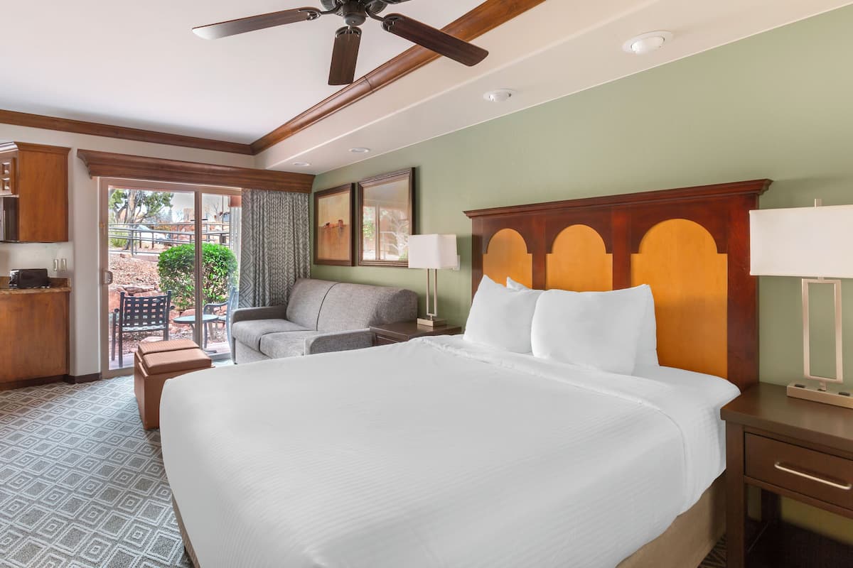 Quarto de hotel com uma cama grande, ventoinha no teto, escrivaninha e vista para o pátio externo.
