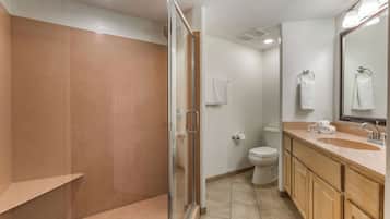 A bathroom with a glass-enclosed shower, a toilet, and a sink with a mirror.