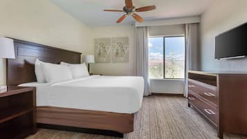 A hotel room with a bed, a ceiling fan, a TV, a dresser, and artwork on the wall.